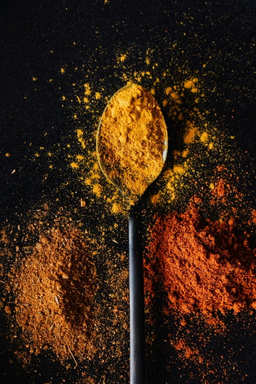 a spoon full of spices sitting on top of a table, a digital rendering, by Adam Marczyński, trending on unsplash, color palette is dark orange, yellow charcoal, exploding powder, medium closeup