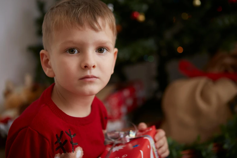 a young boy holding a christmas present in front of a christmas tree, pexels contest winner, sad look, avatar image, toys, medium close up portrait