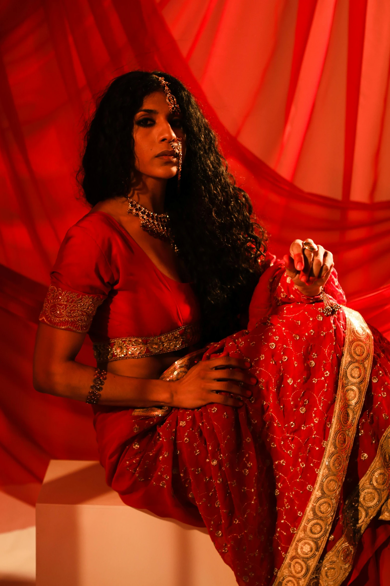 a woman in a red sari posing for a picture, an album cover, cinematic and dramatic red light, ornate clothing, ( ( theatrical ) ), sza