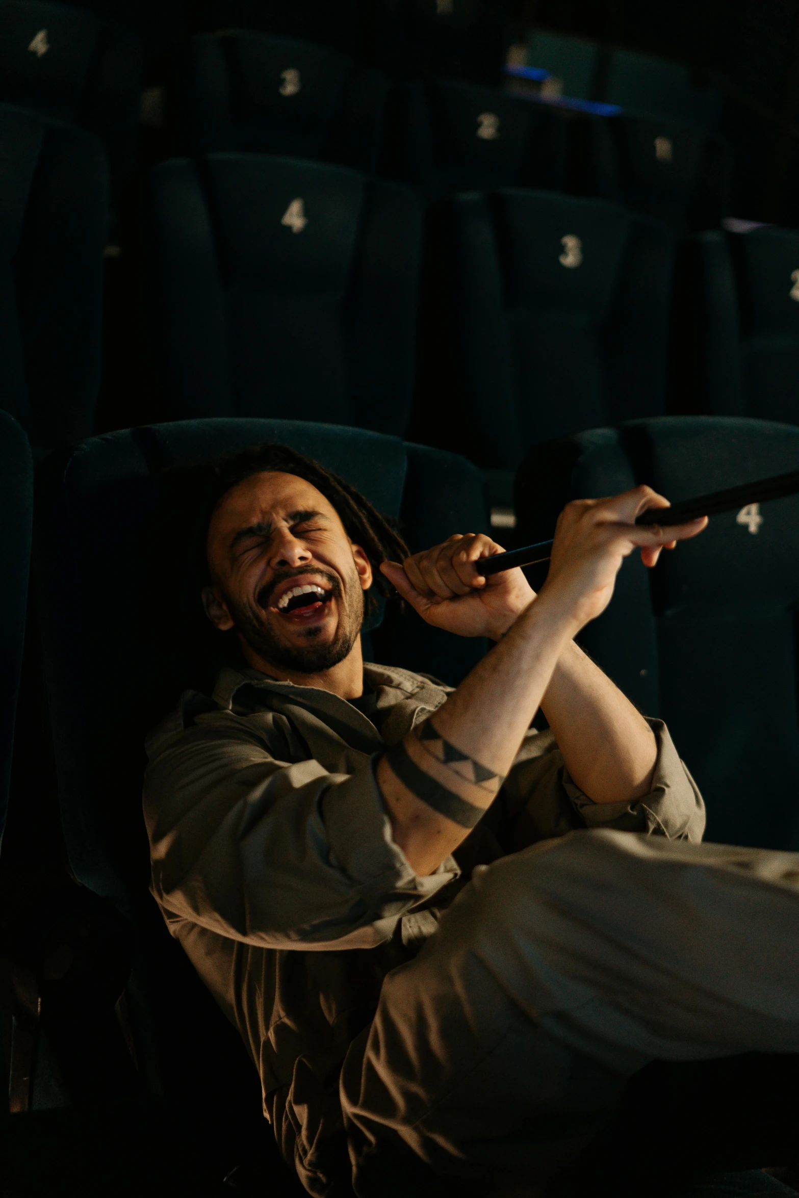 a man sitting in a theater holding a remote, pexels contest winner, renaissance, dramatic wielding gun pose, mutahar laughing, still from loki ( 2 0 2 1 ), zack de la rocha