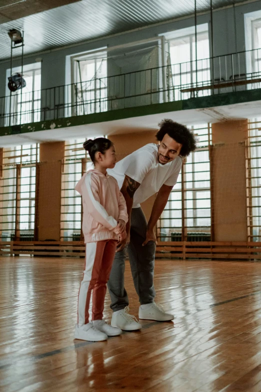 a man standing next to a little girl on a basketball court, pexels contest winner, interactive art, standing in a large empty hall, smiling at each other, ( ( theatrical ) ), teaching