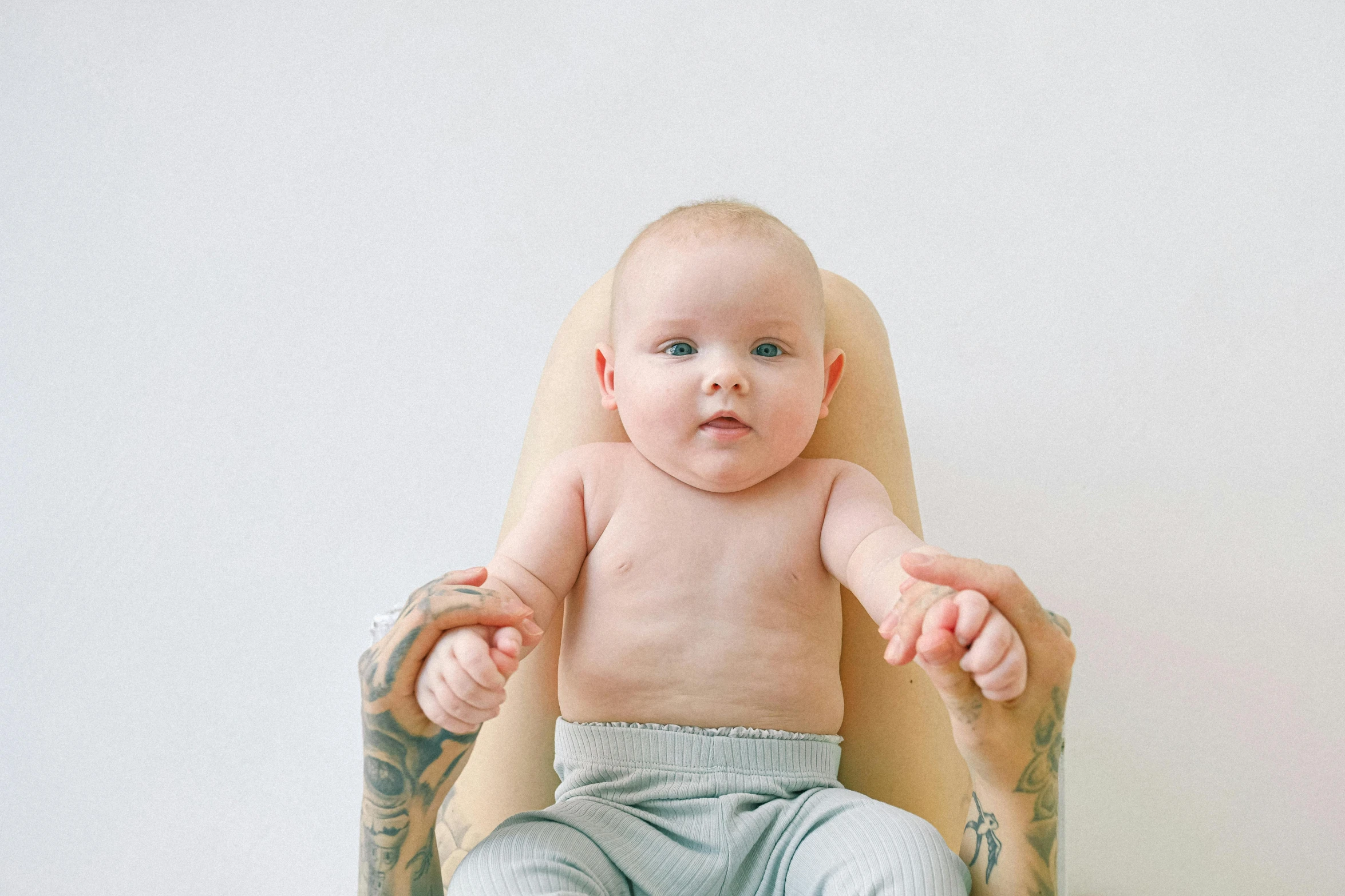 a baby is sitting in a high chair, an album cover, pexels, symbolism, tattooed skin, pale bluish skin, 1 2 9 7, old and young