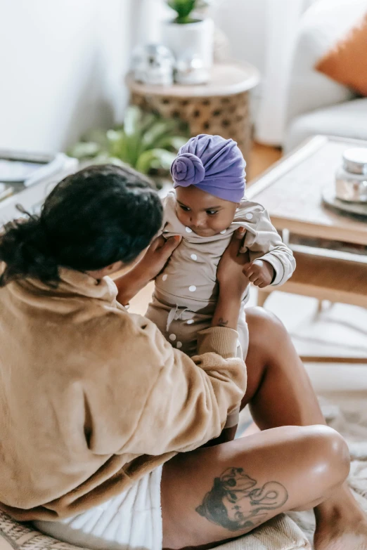 a woman sitting on the floor holding a baby, pexels contest winner, beanie, manuka, thumbnail, wearing a turban