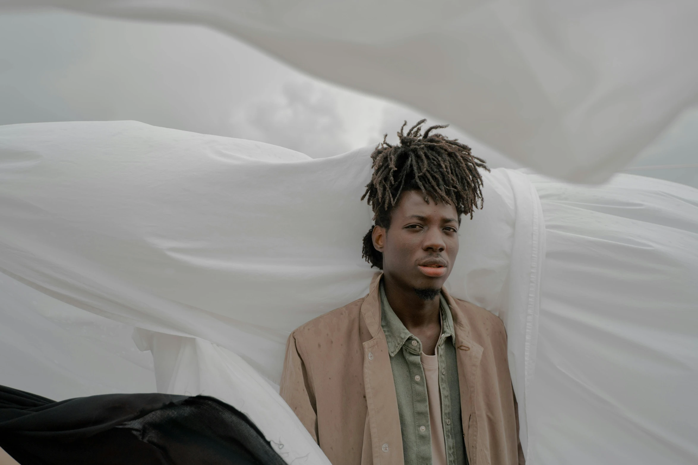 a man with dreadlocks standing in front of a white sheet, by Charles Martin, pexels contest winner, afrofuturism, taupe, male teenager, overcast skies, roots and hay coat