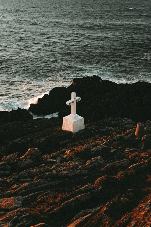 a cross sitting on top of a rock next to the ocean, profile image