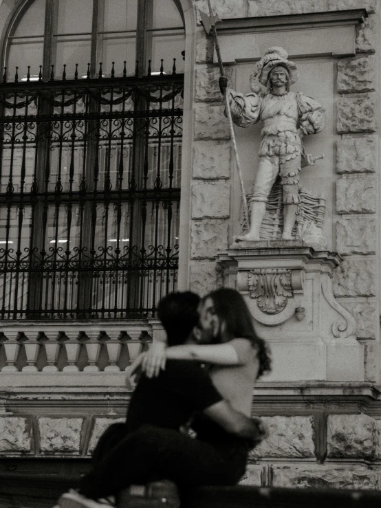 a couple sitting on a bench in front of a building, a black and white photo, by Luis Molinari, pexels contest winner, renaissance, hugging each other, promo image, conquistador, monument