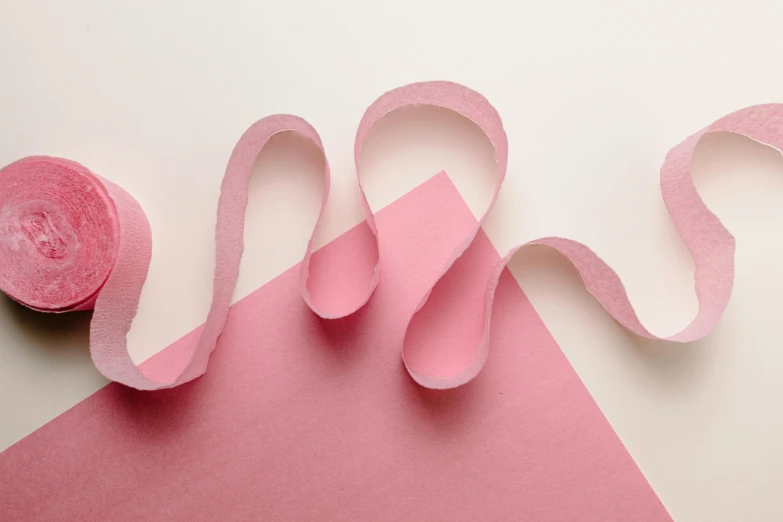 a roll of pink tape sitting on top of a pink piece of paper, inspired by Jean Arp, trending on pexels, serpentine pose, cream paper, ribbon, low detail