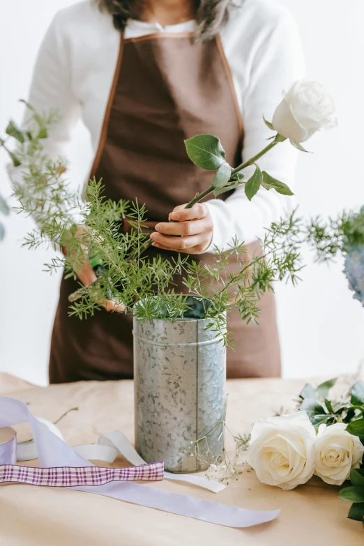 a woman arranging flowers in a vase on a table, featured on pinterest, silver and muted colors, commercially ready, romantic greenery, centerpiece