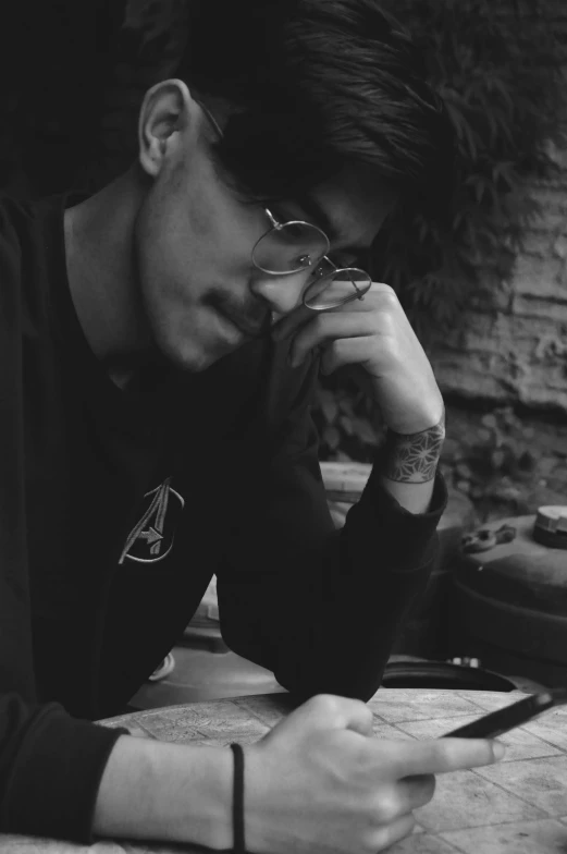 a black and white photo of a man sitting at a table, inspired by Luca Zontini, loish and wlop, with black eyeglasses, profile picture 1024px, androgynous person