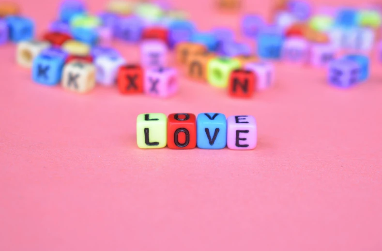 the word love spelled with colorful cubes on a pink background, a macro photograph, by Lorraine Fox, trending on pexels, letterism, miniatures, beads, queer, uwu