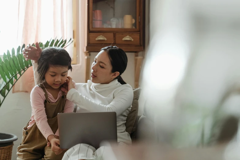 a woman and a little girl sitting on a couch with a laptop, pexels, hurufiyya, teaching, te pae, crying and reaching with her arm, asian woman