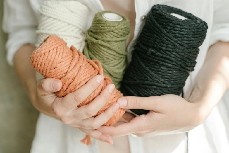 a woman holding three spools of yarn in her hands, trending on unsplash, black and terracotta, webbing, lush vista, close-up product photo