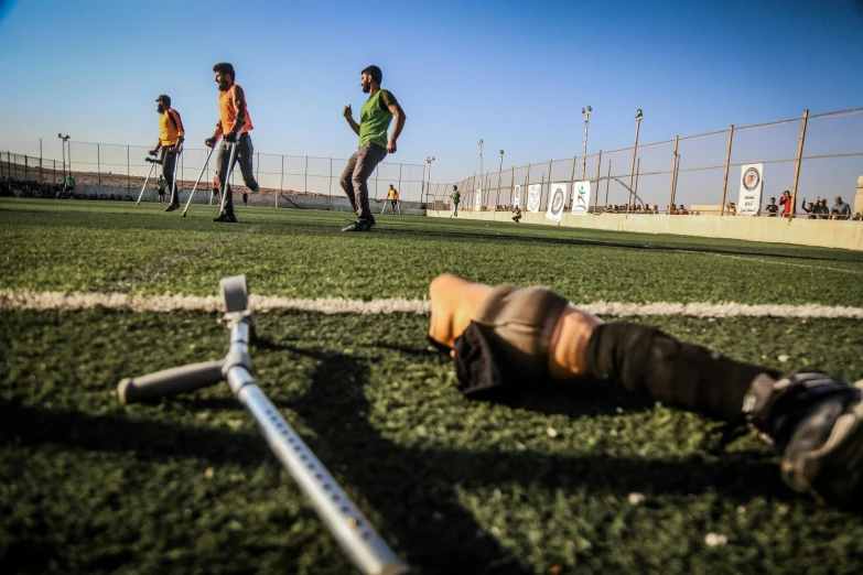 a baseball player laying on the ground next to a bat, by Ibrahim Kodra, happening, one legged amputee, iraq nadar, on a soccer field, photograph taken in 2 0 2 0