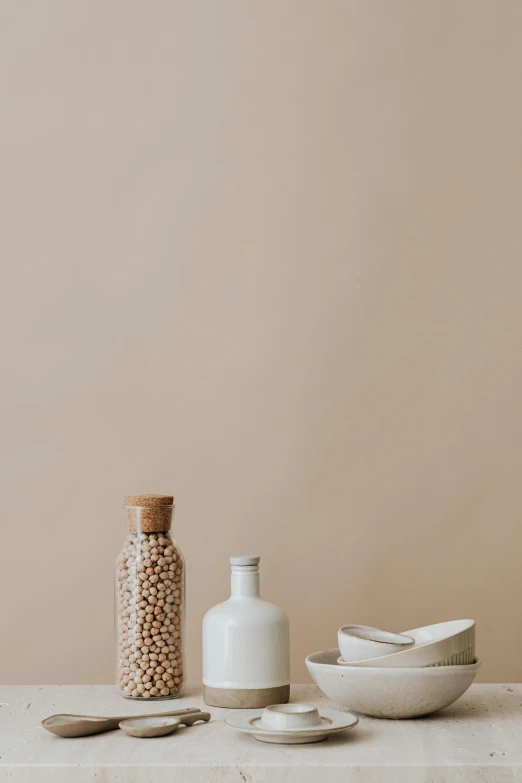 a table topped with bowls and spoons next to a bottle, trending on unsplash, minimalism, pearls, beige colors, illustration, beans