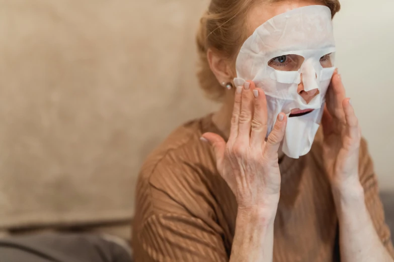 a woman putting a facial mask on her face, by Julia Pishtar, looking old, wearing translucent sheet, drama masks, exclusive
