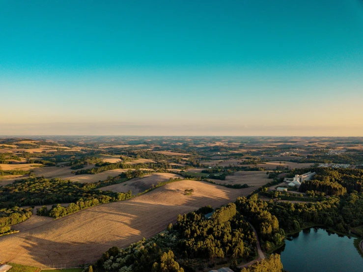 a hot air balloon flying over a lush green field, by Peter Churcher, pexels contest winner, wide river and lake, panorama distant view, golden hour photo, wide view of a farm