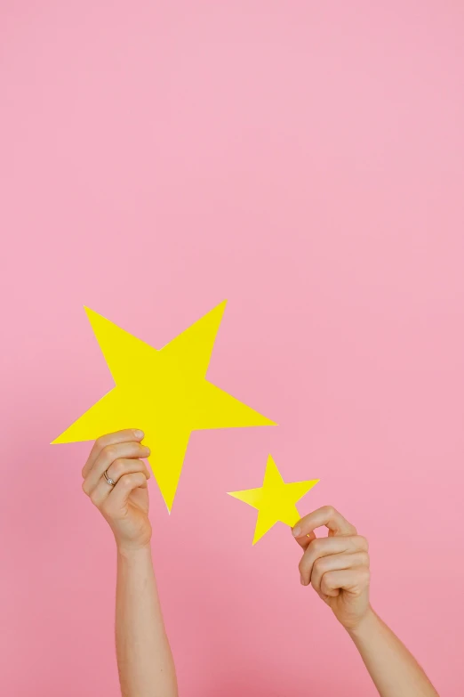 two people holding up yellow stars against a pink background, a photo, by Julia Pishtar, without text, instagram post, solid background, item