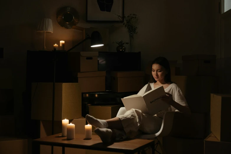 a woman sitting in a chair reading a book, by Shang Xi, pexels contest winner, minimalism, candlelight, cardboard, still from a live action movie, natural light in room