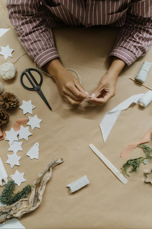a woman sitting at a table making christmas decorations, pexels contest winner, process art, brown paper, star craft, thumbnail, ribbon