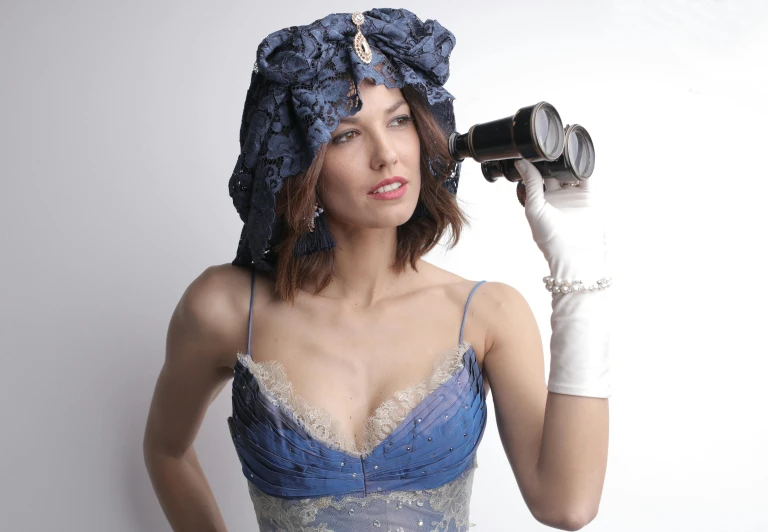 a woman in a blue dress holding a camera, inspired by Harrison Fisher, rococo onyx headpiece, push-up underwire. intricate, model is wearing techtical vest, alessandra ambrosio