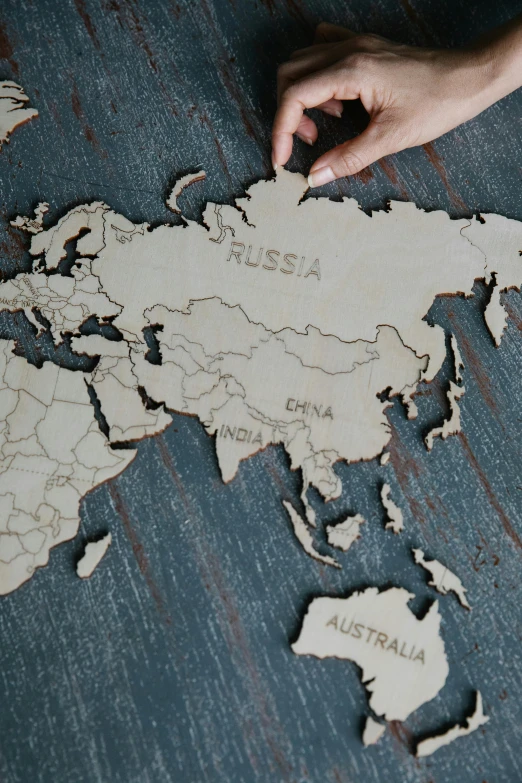 a person pointing at a wooden world map, a jigsaw puzzle, by Julia Pishtar, engraved, asian, with names, overview