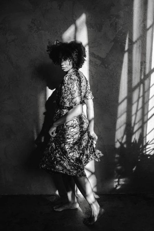 a black and white photo of a woman standing in front of a window, inspired by Carrie Mae Weems, renaissance, dressed in a flower dress, intense shadows, sza, leaning against the wall