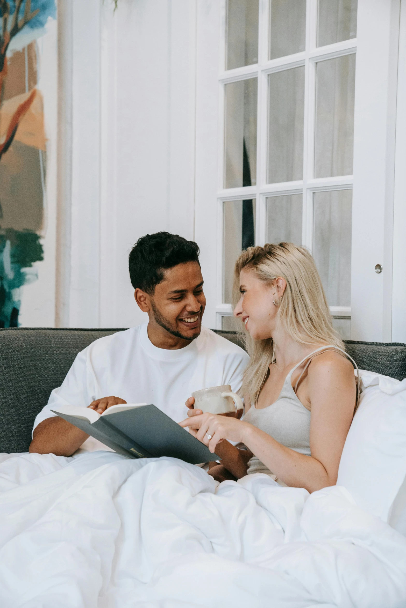 a man and woman sitting on a bed looking at a tablet, by Cosmo Alexander, pexels contest winner, reading the book about love, smiling at each other, white bed, gif