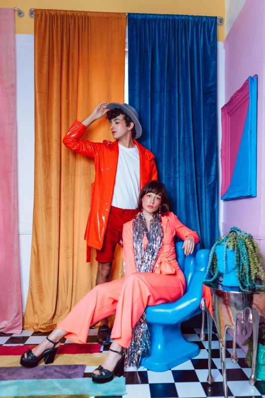 a couple of women sitting on top of a blue chair, an album cover, trending on pexels, neo-fauvism, wearing a colorful men's suit, shot in the photo studio, declan mckenna, avant garde coral