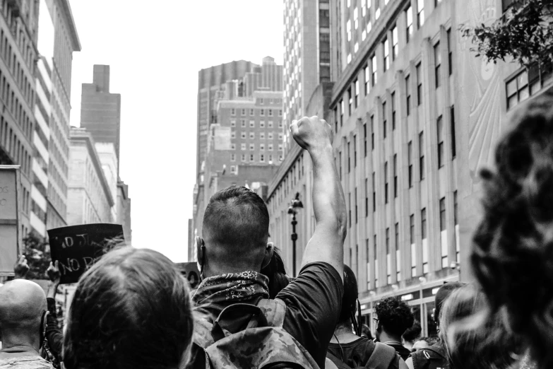 a crowd of people walking down a city street, a black and white photo, pexels, sots art, one fist raised high in triumph, attacking nyc, a man wearing a backpack, looking threatening