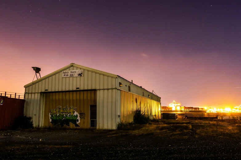 a building sitting in the middle of a field, unsplash, graffiti, spaceport docking bay at night, mining outpost, golden hour photo, night time footage