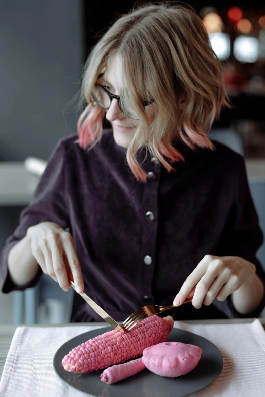 a woman sitting at a table with a plate of food, trending on pexels, process art, pink wispy hair, chocolate frosting, holds a small knife in hand, gif