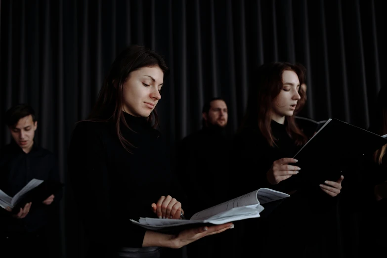 a group of people standing in front of a black curtain, an album cover, by Emma Andijewska, pexels contest winner, sheet music, worship, ignant, performing