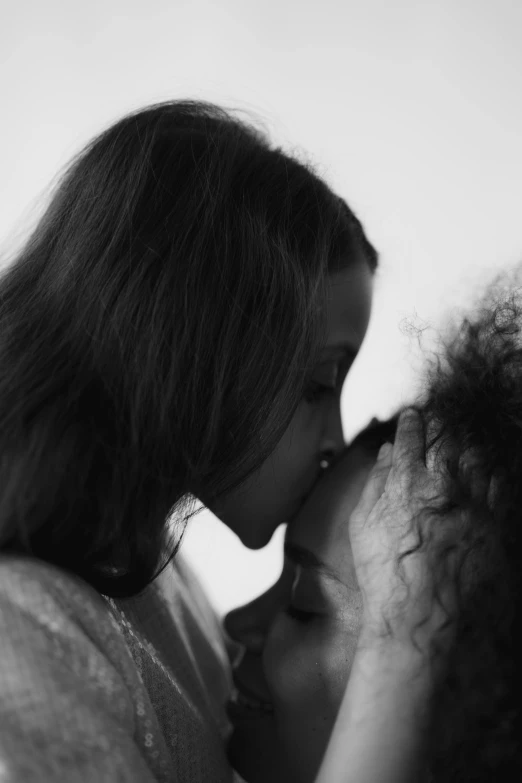 a black and white photo of a mother kissing her daughter, inspired by Nan Goldin, antipodeans, frank dillane, curly hair, morning. hyperrealism, aurora aksnes and zoë kravitz