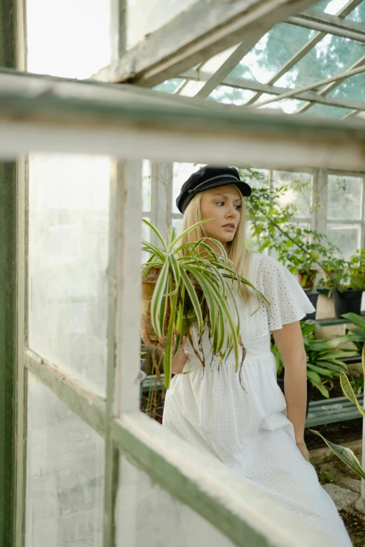 a woman standing in a greenhouse holding a potted plant, inspired by Elsa Bleda, unsplash, renaissance, wearing newsboy cap, dakota fanning, white clothing, portrait image