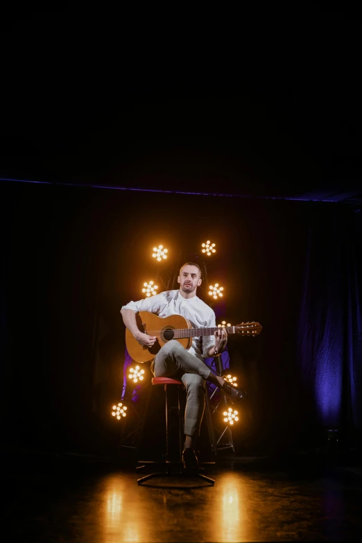 a man sitting on a chair playing a guitar, inspired by James Morrison, light and space, light show, looking towards camera, flowers around, episode