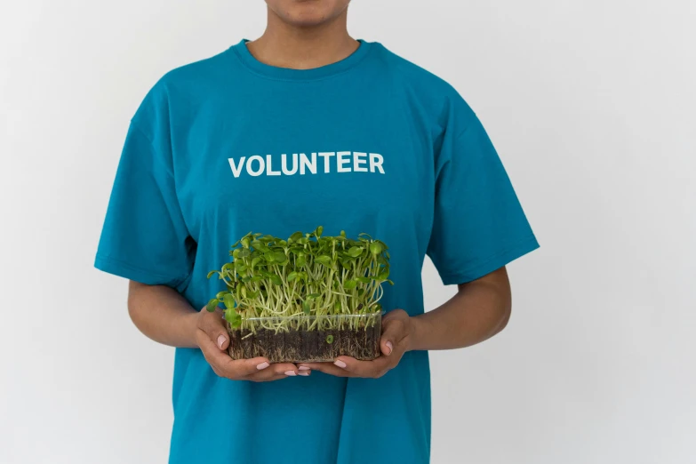 a boy in a volunteer t - shirt holding a tray of sprouts, an album cover, unsplash, teal uniform, avatar image, lush plant growth, close-up photo