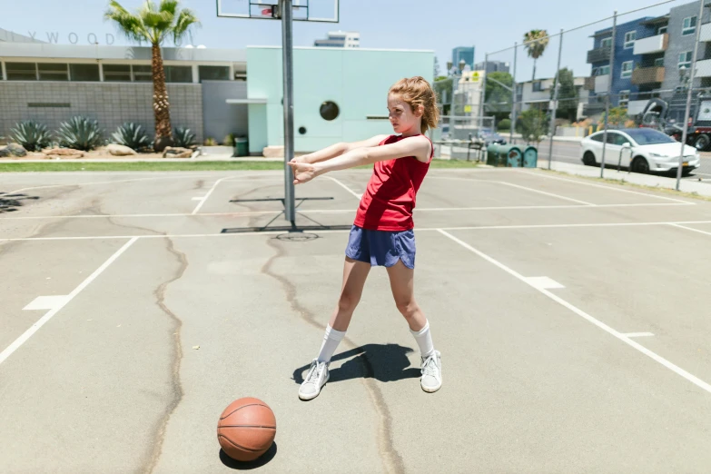 a little girl standing on top of a basketball court, by Josh Bayer, dribble contest winner, sadie sink, wearing red shorts, action shots, on the concrete ground