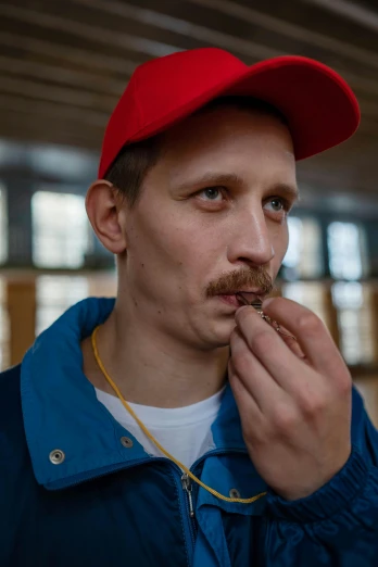a man in a red hat eating a donut, by Julia Pishtar, with trimmed mustache, in russia, non binary model, wearing a navy blue utility cap