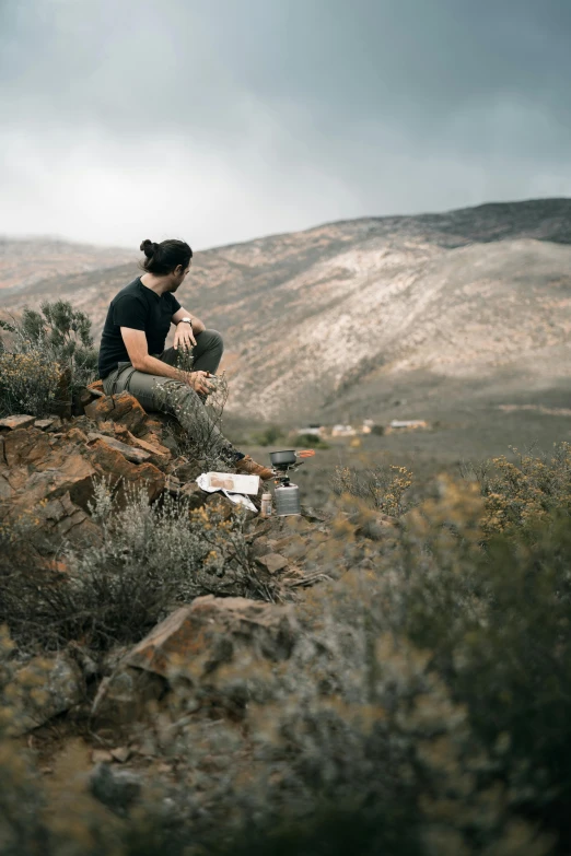 a man sitting on top of a rocky hill, by Lee Loughridge, unsplash contest winner, plein air, letterboxing, side profile shot, in a valley, dessert