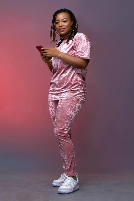 a woman standing with a cell phone in her hand, an album cover, by Chinwe Chukwuogo-Roy, trending on pexels, pink clothes, full body with dynamic pose, wearing pajamas, very reflective