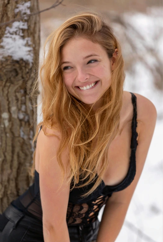 a woman posing next to a tree in the snow, she is wearing a black tank top, sydney sweeney, beautiful smiling face, uncropped