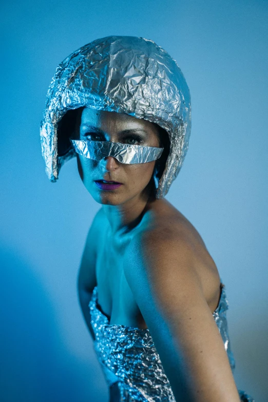 a woman in a silver dress and a helmet, inspired by hajime sorayama, unsplash, cold studio lighting, blue, in a space cadet outfit, modelling