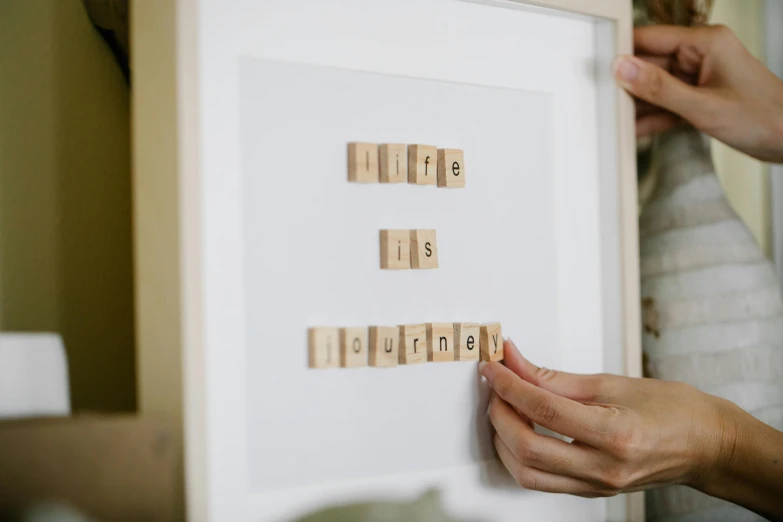 a close up of a person holding a scrabble board, a picture, inspired by Ian Hamilton Finlay, picture frames, journey, in white lettering, magnetic