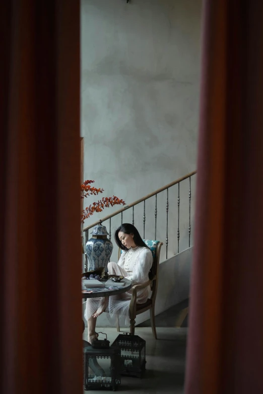 a woman sitting in a chair reading a book, inspired by Tang Yin, unsplash, visual art, cinematic style photograph, ao dai, porcelain, indoor scene