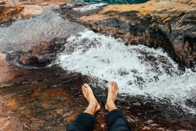 a person standing on top of a rock next to a river, an album cover, by Jessie Algie, trending on unsplash, real human feet, wet amphibious skin, sitting relax and happy, on a hot australian day