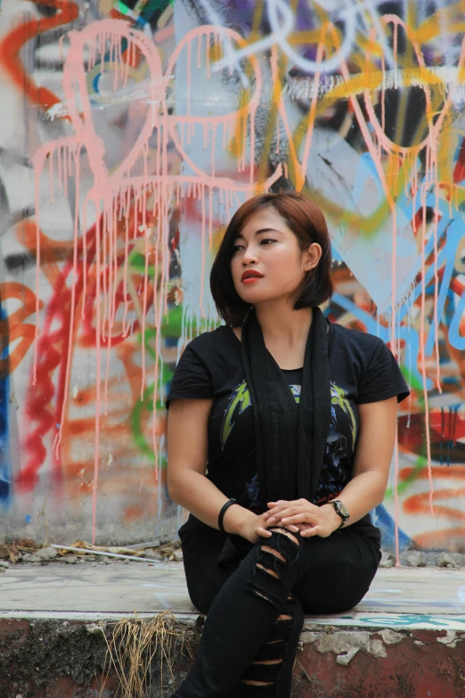 a woman sitting on a ledge in front of a graffiti covered wall, an album cover, inspired by Ruth Jên, wearing a black shirt, malaysian, ((portrait)), trending photo