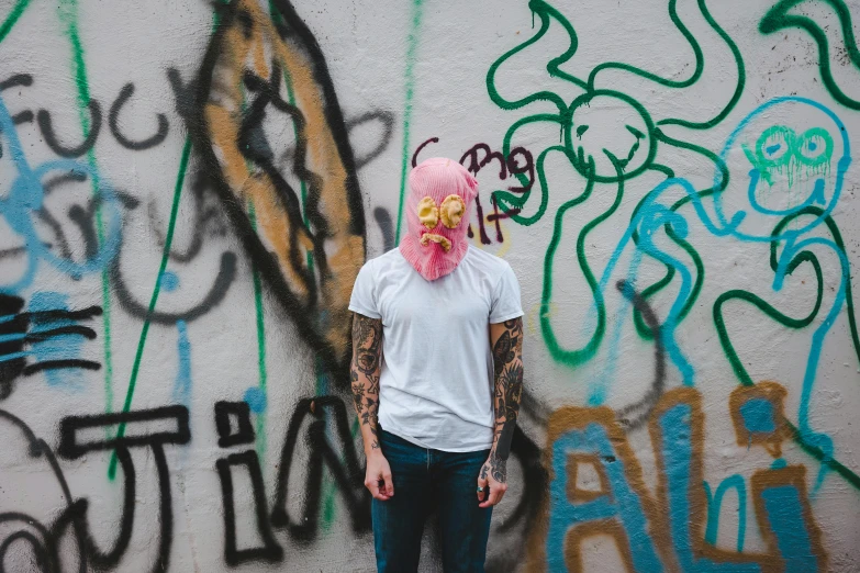 a person standing in front of a wall covered in graffiti, a photo, pexels contest winner, pink face, super hero mask, hipster, meth head