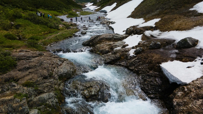 a group of people standing on top of a snow covered mountain, by Daniel Seghers, pexels contest winner, hurufiyya, flowing clear water creek bed, nordic summer, thumbnail, small creek