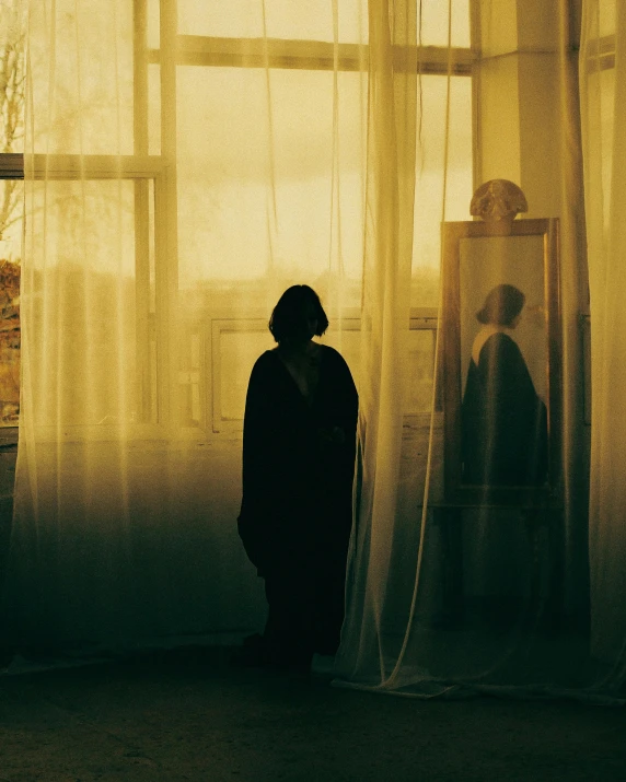 a silhouette of a person standing in front of a window, poster art, pexels contest winner, tonalism, yellow robe, jan saudek, rinko kawauchi, with a mirror