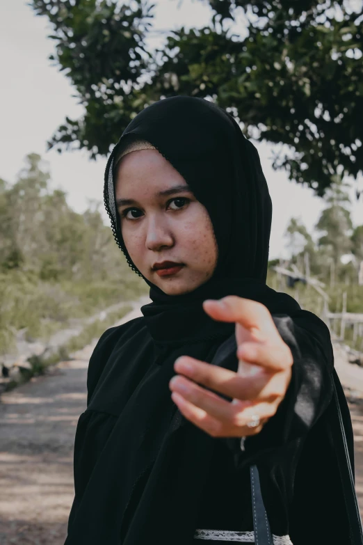 a woman in a black hijab holding a cell phone, an album cover, inspired by Bernardino Mei, unsplash, in a fighting stance, malaysian, young angry woman, grainy